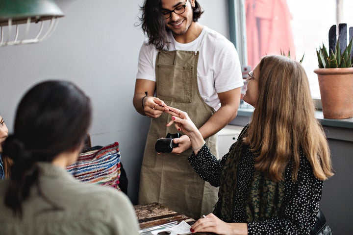 Woman giving credit card to smiling waiter at restaurant