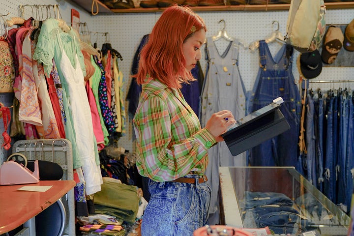 Asian woman running a secondhand store is checking inventory using a tablet