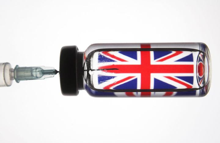 A medical syringe and a vial seen in front of the Union Jack