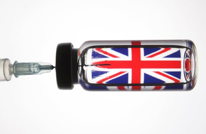 A medical syringe and a vial seen in front of the Union Jack