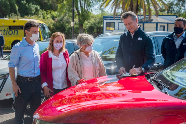 On the hood of an electric car, California Gov. Gavin Newsom signs an executive order requiring all new passenger vehicles sold in the state to be zero-emission by 2035 after a press conference on Sept. 23, 2020, at Cal Expo in Sacramento.