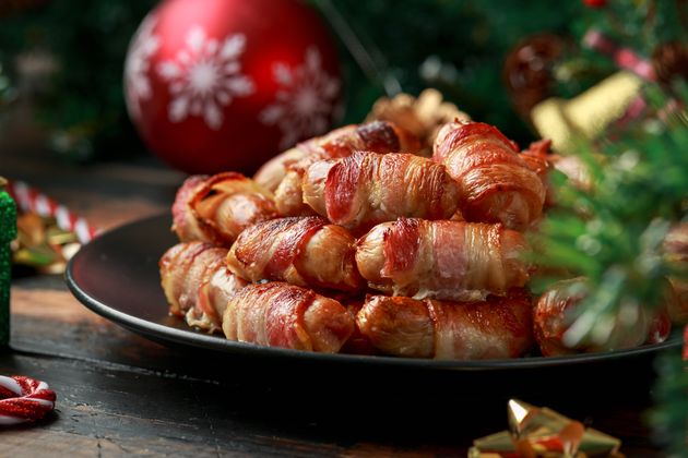 Christmas Pigs in blankets, sausages wrapped in bacon with decoration, gifts, green tree branch on wooden rustic table.