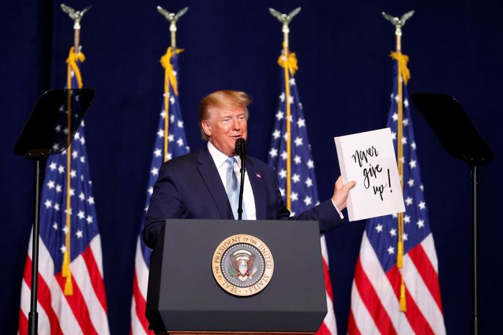 Trump holds a sign that reads, "Never give up!" as he speaks to evangelical supporters in Miami on Jan. 3, 2020.