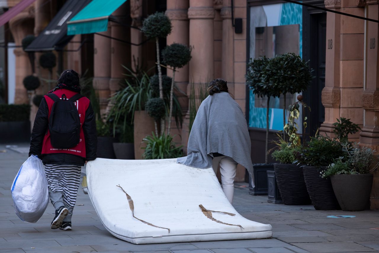 Two rough sleepers drag a mattress down the road in London's Mayfair in November