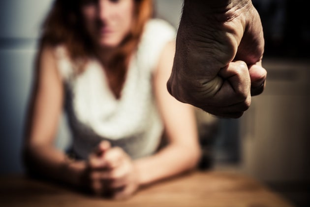 Young woman is sitting hunched at a table at home, the focus is on a man's fist in the foregound of the image