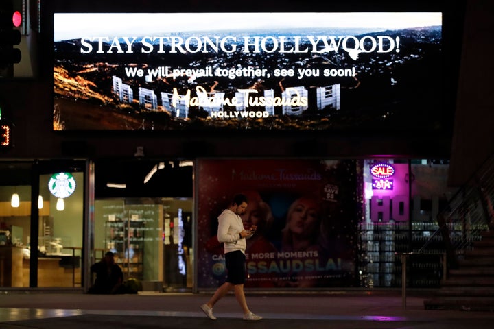 A man walks under a sign that reads "Stay Strong Hollywood" along Hollywood Boulevard on Thursday, April 2, 2020, in Los Angeles. California is in its second week of a statewide lockdown, where schools and nonessential businesses are closed and the governor has ordered people to stay home. (AP Photo/Marcio Jose Sanchez)