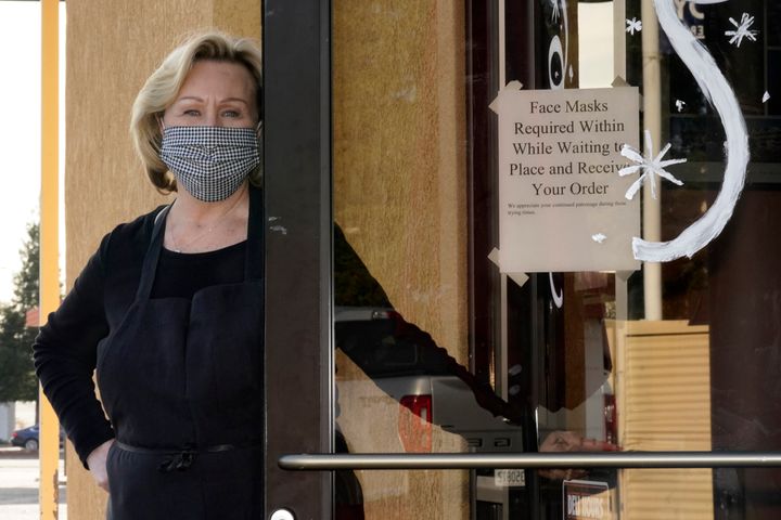 Brenda Luntey, poses for a photo by a sign advising customers to wear face masks that is posted on the door of the San Francisco Deli in Redding, Calif., on Dec. 3, 2020. 