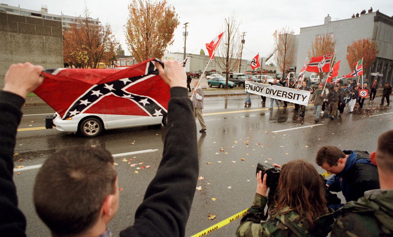 An unidentified supporter waves a Confederate flag while members of the Aryan Nations carry Nazi flags and a banner saying "Enjoy Diversity" during a parade in downtown Coeur d'Alene, Idaho, on Oct. 28, 2000.