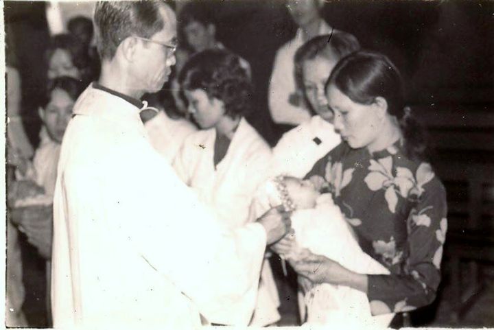 The writer, two months old at the time, is baptized held in her mother's arms.