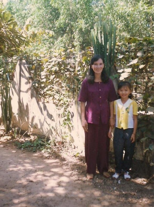 The writer, then about eight years old, stands with her mother outside their home in Vietnam.