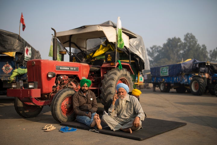 Protesting farmers Raghuvir Singh, right, and Gurnam Singh bask in the morning sun while sitting next to their tractor parked on a highway, during a protest at the Delhi-Haryana state border, India, on Dec. 1, 2020.