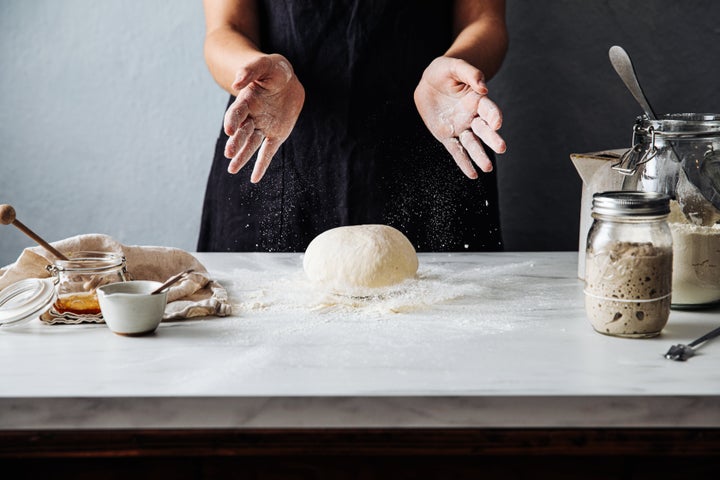 Midsection of woman throwing dough on flour over marble counter. Female is preparing sourdough bread. She is in kitchen.