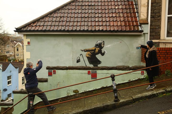 Συνοδευμόμενη με το χαρακτηριστικό... "Aachoo!!" η νέα τοιχογραφία του μυστηριώδους αλλά τόσο γοητευτικού street artits Μπάνκσι, απεικονίζει μία γυναίκα που φτερνίζεται δυνατά με αποτέλεσμα να εκτοξευθεί στον αέρα τη μασέλα της! 11 Δεκεμβρίου 2020. / (Photo by GEOFF CADDICK/AFP via Getty Images)