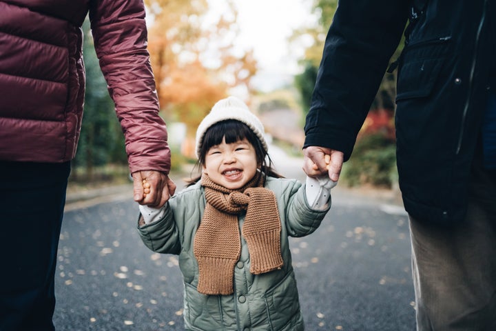 An adorable and happy little girl holding her grandparent's hand and having a relaxing walk in the park