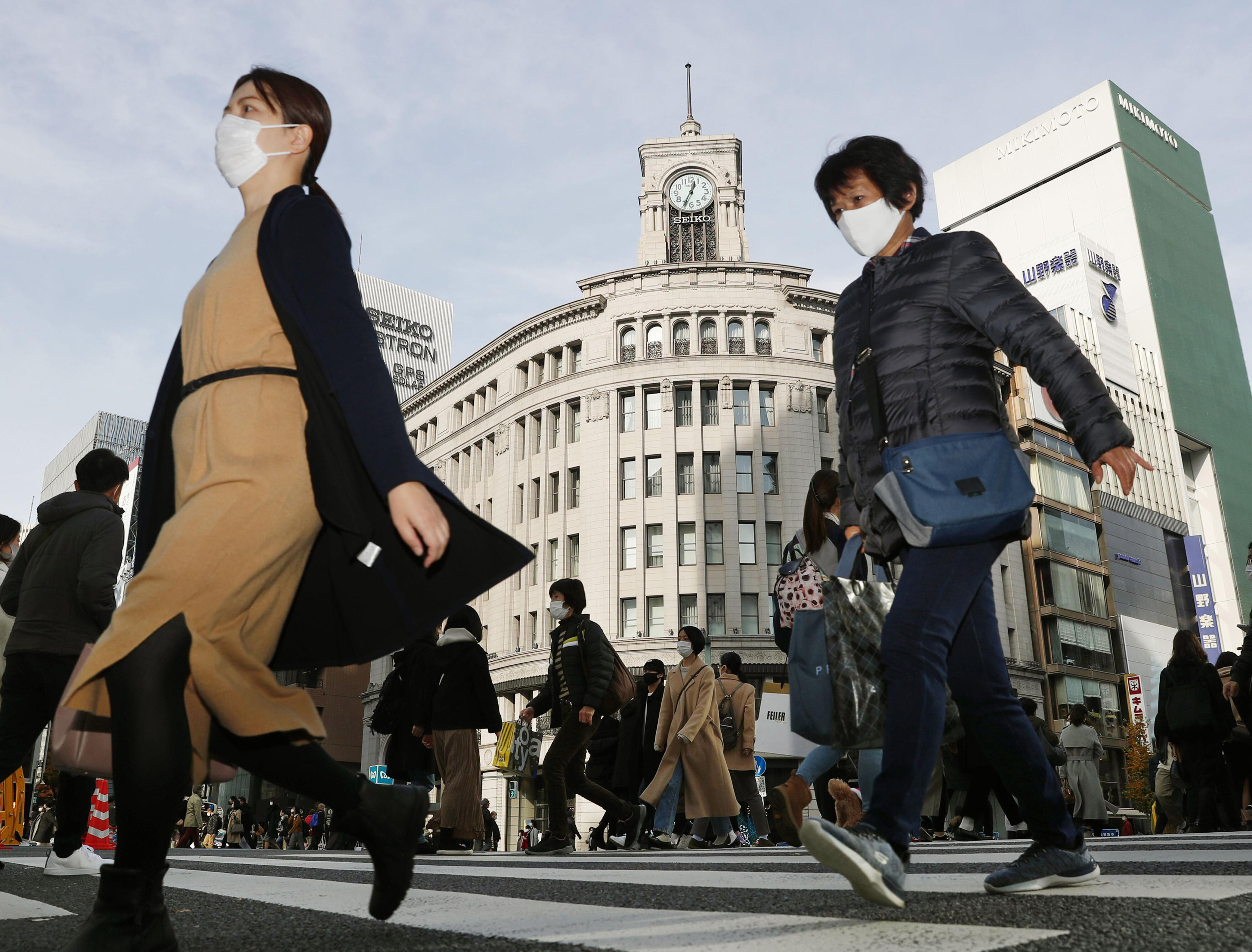 People cross an intersection in Tokyo's Ginza district on December 13, 2020. Japan’s daily coronavirus cases have exceeded 3,000 for the first time while the government delays stricter measures for fear of hurting the economy ahead of the holiday season.