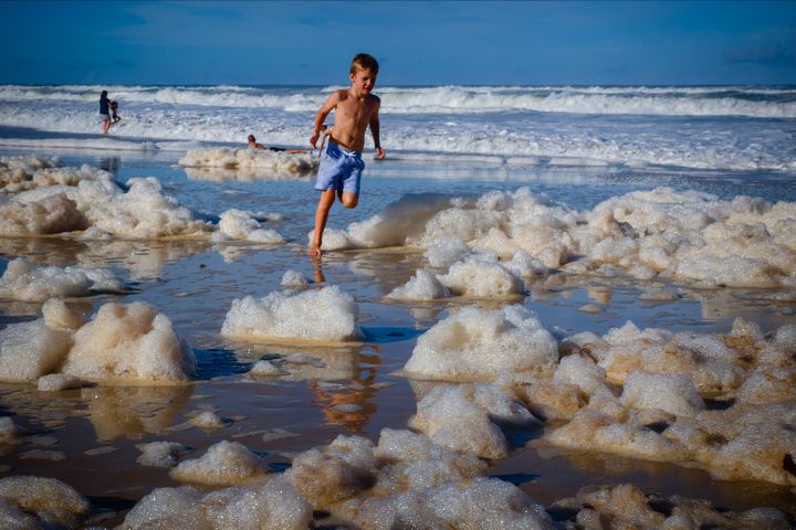 A child plays amongst beach foam in the wake of cyclonic conditions at Currumbin Beach on December 15, 2020, after wild weather lashed Australia's Northern New South Wales and South East Queensland with heavy rain, strong winds and king tides. 