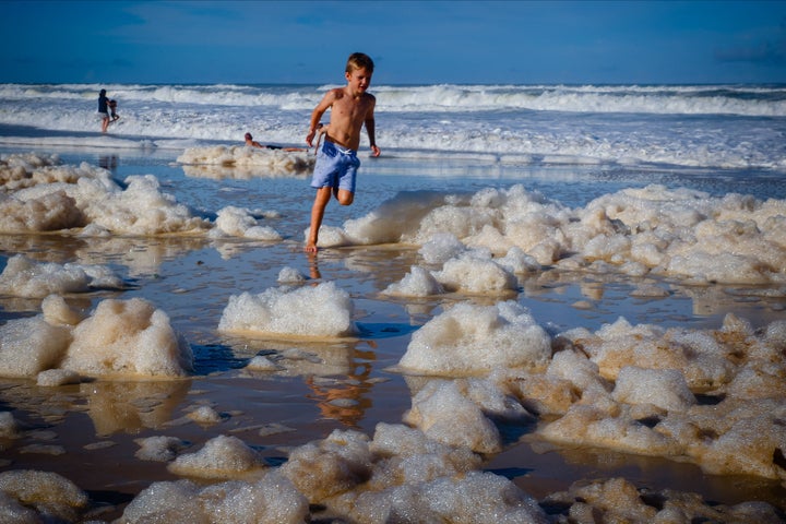 A child plays amongst beach foam in the wake of cyclonic conditions at Currumbin Beach on December 15, 2020, after wild weather lashed Australia's Northern New South Wales and South East Queensland with heavy rain, strong winds and king tides.