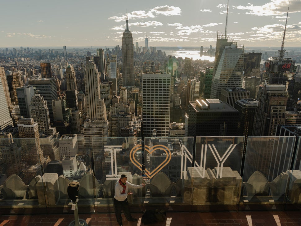 A man posing in front of the "I Heart NY" sign at the observation deck at the Top of the Rock at Rockefeller Center in midtown Manhattan.