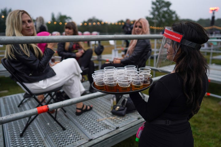 A waitress walks between socially distanced enclosures selling drinks to fans 