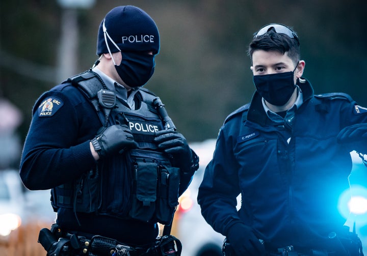 RCMP officers wearing face masks to curb the spread of COVID-19 stand by as protesters opposed to the Trans Mountain pipeline expansion block rail lines in Burnaby, B.C., on Nov. 27, 2020.