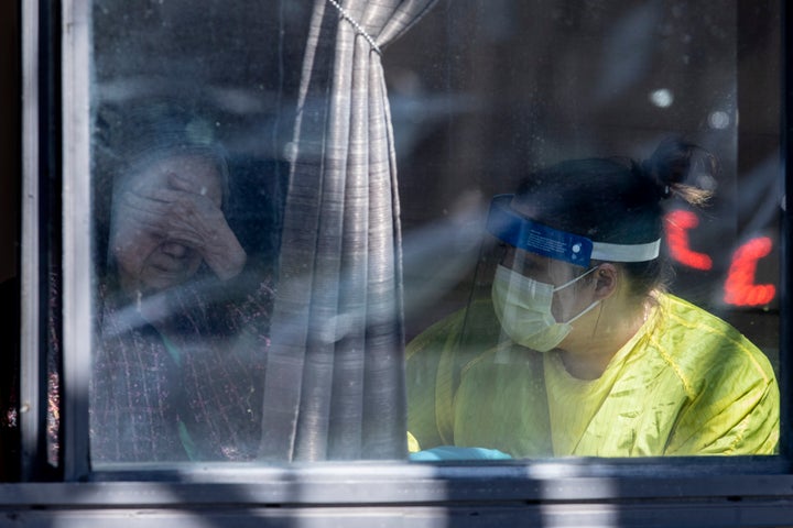 A COVID-19 positive resident, identified as Flora, sits with a member of staff after receiving an absolution from a priest, at Orchard Villa Care home, in Pickering, Ont. on April 25, 2020.