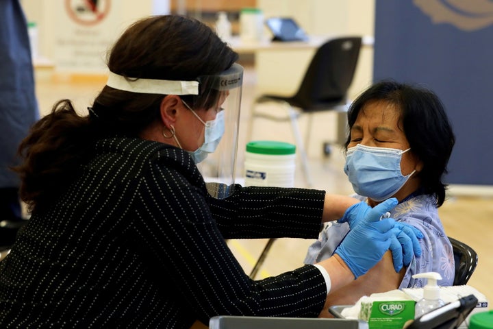 A healthcare worker administers the first dose of the Pfizer and BioNTech COVID-19 vaccine in Ontario to personal support worker Anita Quidangen at The Michener Institute in Toronto on Dec. 14, 2020.