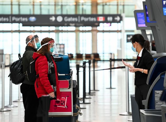 People wear protective equipment as they check in at Pearson International Airport during the COVID-19...