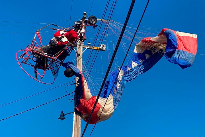 In this photo provided by the California Highway Patrol, a man dressed as Santa Claus who was flying on a powered parachute on his way to deliver candy canes to children is seen stuck on power lines in Rio Linda, Calif., on Sunday, Dec. 20, 2020. The man was rescued uninjured. The incident happened shortly after the man took off near a school in Rio Linda and then hit and became suspended in power lines, a Federal Aviation Administration spokesman told KCRA-TV. (California Highway Patrol via AP)