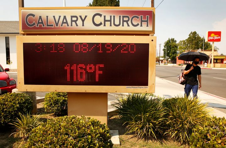 A man with an umbrella for shade walks past the thermometer at Calvary Church in Woodland Hills, California, as it registers 