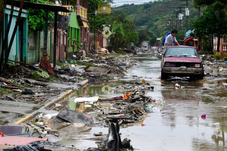 A group of people on a car drive through a mud-covered street with debris caused by Hurricane Iota's flooding on November 21 in San Pedro Sula, Honduras. 