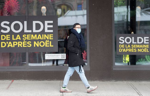 A man wears a face mask as he walks by store window adverstising after Christmas sales on Boxing Day...