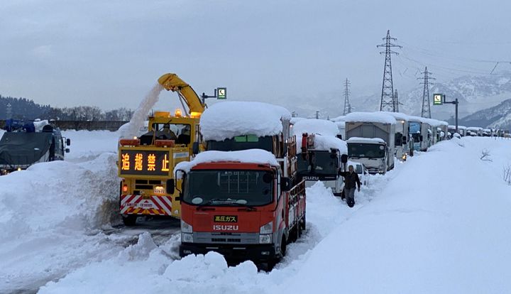 大雪により関越自動車道上り線塩沢石打インター手前で立ち往生した車両の列。左は除雪車＝12月18日、新潟県南魚沼市