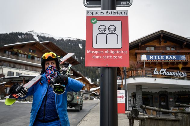 알프스의 유명 스키 관광지인 스위스 베르비에에서 한 스키 관광객이 '외부 공간 마스크 착용'을 알리는 안내판 앞을 지나고 있다. 2020년
