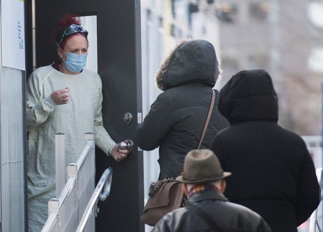 A healthcare worker talks with people as they wait to be tested for COVID-19 at a clinic in Montreal...