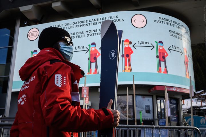 A ski instructor walks past a giant screen reading in French: "Mask mandatory in the queues, and the ski lifts, distance of at least 1.5m in queues" at the start of a ski lift in the Alpine resort of Verbier.