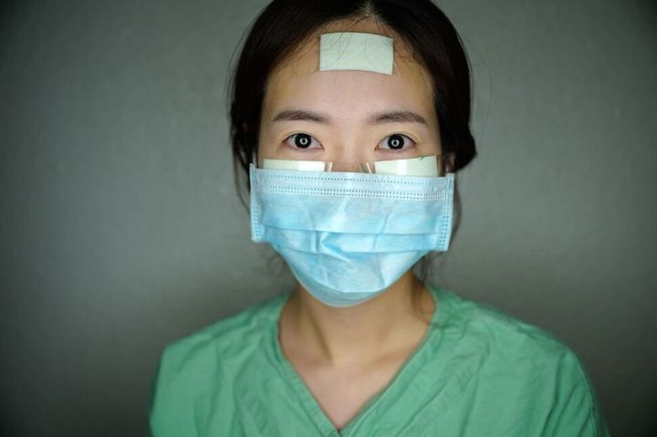 大邱市の啓明大学病院で働く看護師ユン・ナヨン氏。3月12日、交代制で働く合間の休憩時間にカメラの前に立ってくれた。コロナウイルス患者をケアする看護師たちは全身防護服（PPE）を何時間も着続け、顔に絆創膏を貼ることによりマスクの長時間の着用による痛みを防いでいる