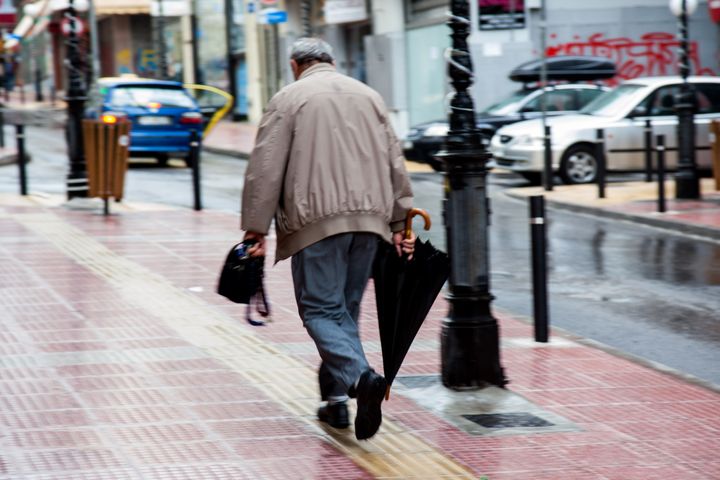 An old man walks after the rain on the streets. (Photo by Konstantinos Zilos/NurPhoto via Getty Images)