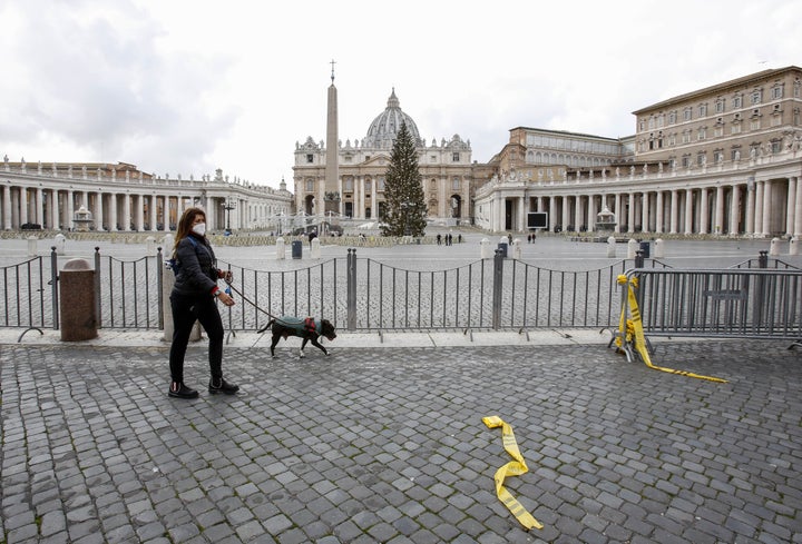 A woman wearing a face mask walks with her dog outside of an empty St. Peter's Square at the Vatican, December 25, 2020. 