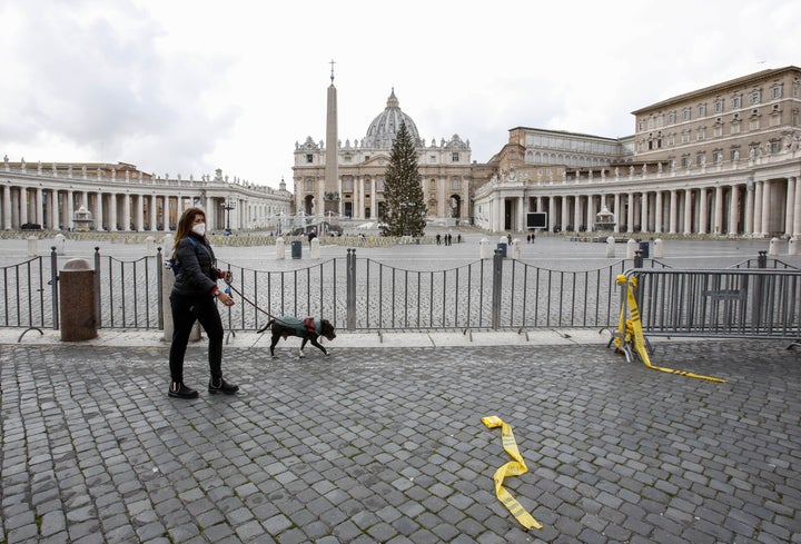 A woman wearing a face mask walks with her dog outside of an empty St. Peter's Square at the Vatican, December 25, 2020. 