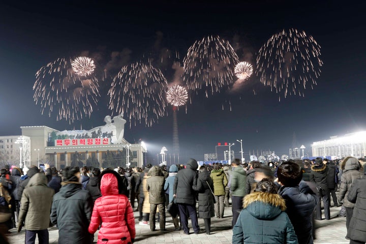 A fireworks display decorates the night sky to celebrate the New Year, as crowds of people look on, at Kim Il Sung Square in 