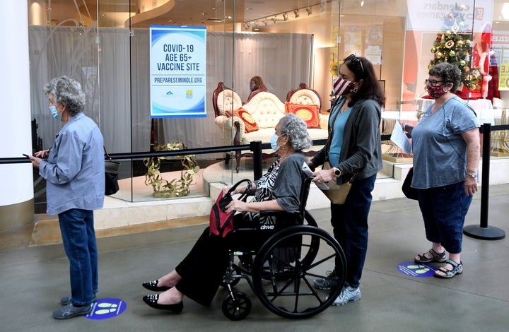 People wait in a line on New Year's Eve to receive a COVID-19 vaccination at a site for seniors in an unoccupied store at the