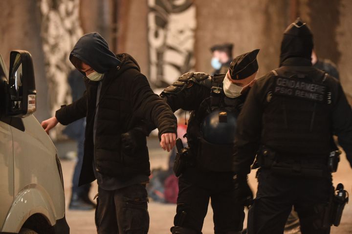 French Gendarmes pat down a reveller after breaking up a rave near a disused hangar in Lieuron.