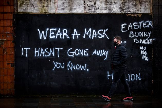 A man wearing a face covering walks past graffiti on the Lower Newtownards Road in Belfast with a message reading: 