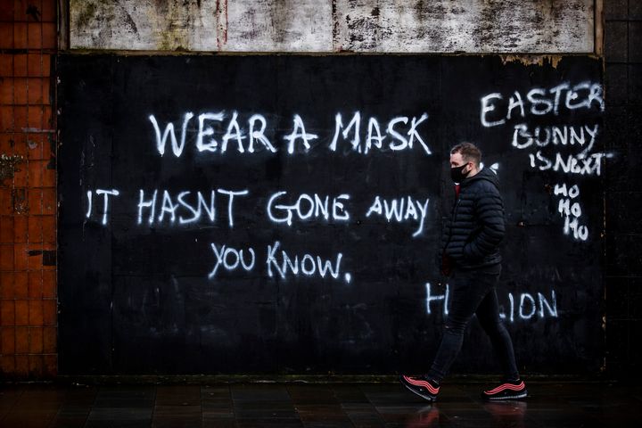 A man wearing a face covering walks past graffiti on the Lower Newtownards Road in Belfast with a message reading: "Wear a mask. It hasn't gone away you know."