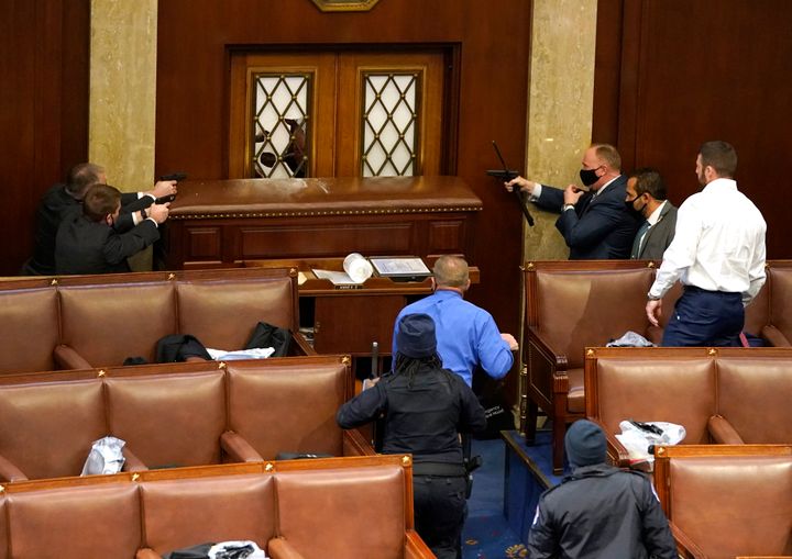 US Capitol police officers point their guns at a door that was vandalised in the House Chamber during a joint session of Congress.