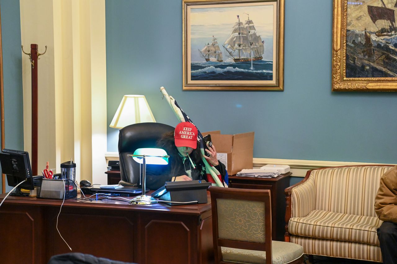 A rioter wearing a "Keep America Great" hat sits in Pelosi's office suite.