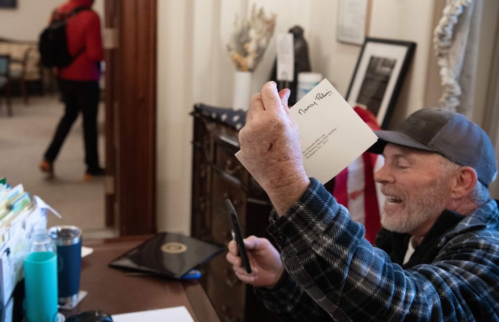 A pro-Trump rioter goes through items on the desk of a Pelosi staffer.