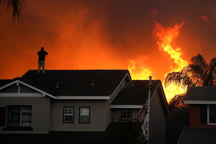 Herman Termeer, 54, stands on the roof of his home as the Blue Ridge Fire burns along the hillside in Chino Hills, Calif., on Oct. 27, 2020. 