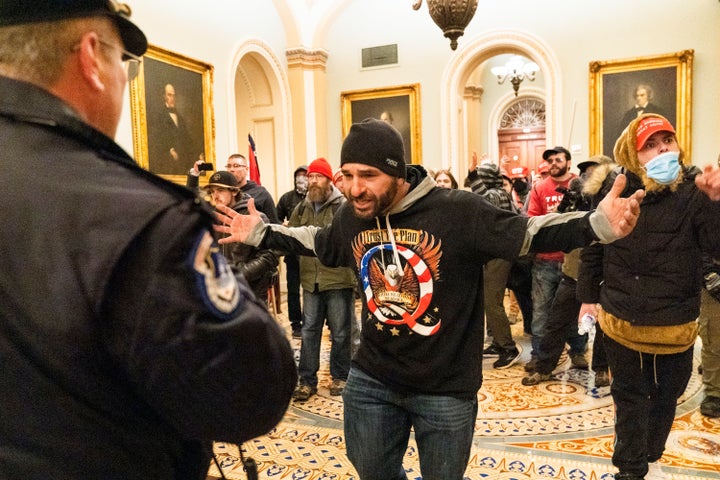 Un partisan de Donald Trump, vu portant une chemise QAnon, se confronte à des officiers de la police du Capitole devant la salle du Sénat.