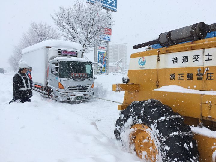 立ち往生が続く国道8号で、国土交通省の重機にけん引されるトラック（左）＝2018年2月8日、福井市 
